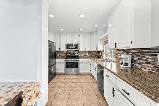 kitchen featuring sink, appliances with stainless steel finishes, white cabinetry, light tile patterned flooring, and dark stone counters