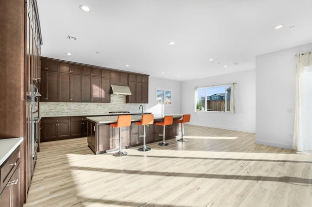 kitchen featuring dark brown cabinetry, a breakfast bar, a center island with sink, and light wood-type flooring