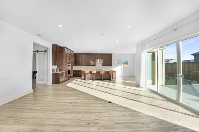 unfurnished living room with a barn door and light hardwood / wood-style flooring