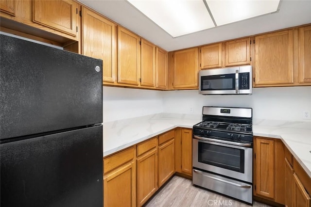 kitchen with light hardwood / wood-style flooring, light stone countertops, and stainless steel appliances