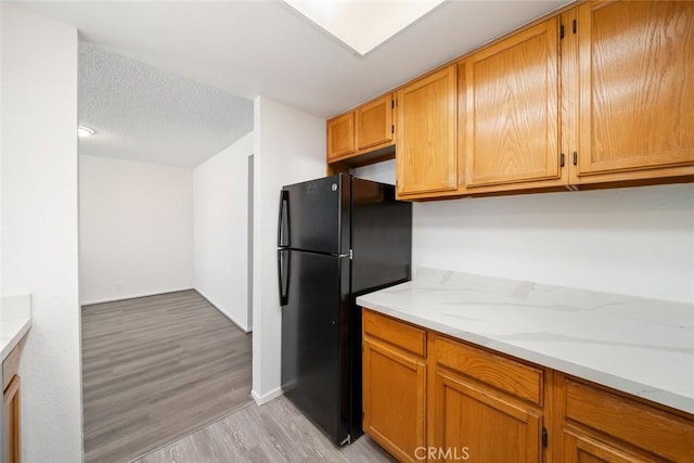 kitchen with light stone countertops, a textured ceiling, black fridge, and light wood-type flooring