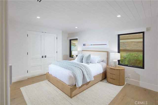 bedroom with light wood-type flooring, wood ceiling, and a closet