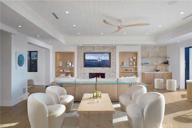 living room featuring built in features, light wood-type flooring, a tray ceiling, a fireplace, and wooden ceiling