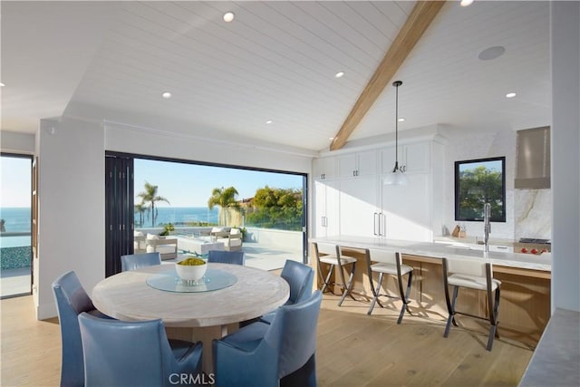 dining room featuring plenty of natural light, light hardwood / wood-style flooring, lofted ceiling with beams, and a water view