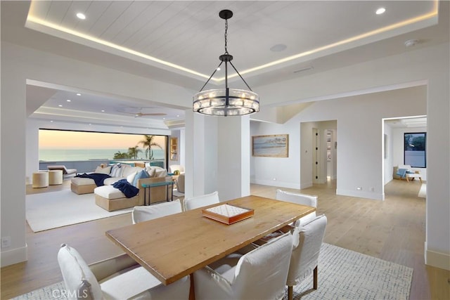 dining area with light hardwood / wood-style floors, a tray ceiling, and a chandelier