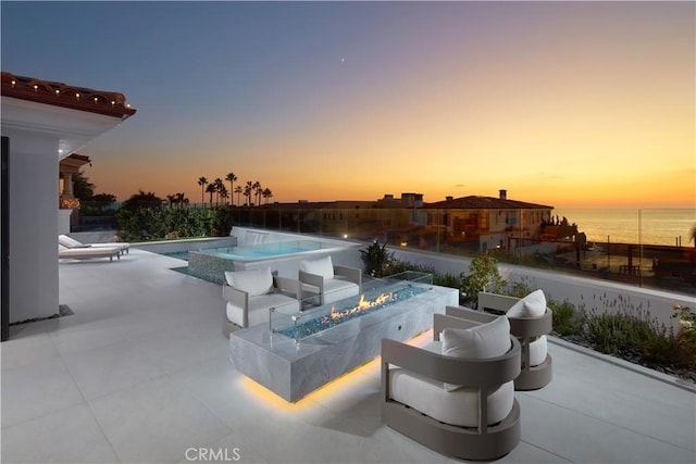 pool at dusk with a water view, a patio area, and a fire pit