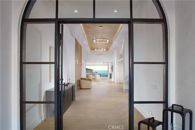 hallway with a tray ceiling, light hardwood / wood-style flooring, french doors, and expansive windows