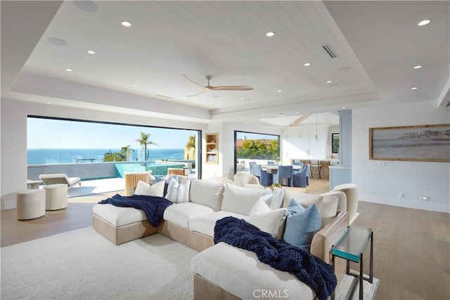 living room with wood ceiling, light wood-type flooring, a water view, a raised ceiling, and ceiling fan