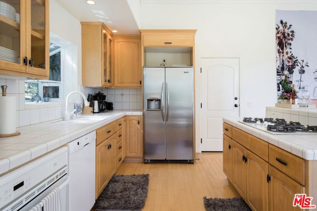 kitchen with tile countertops, sink, backsplash, light hardwood / wood-style floors, and white appliances