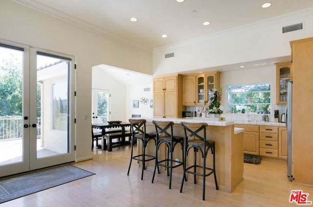 kitchen with french doors, a kitchen bar, crown molding, and light brown cabinetry