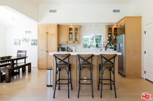 kitchen with light hardwood / wood-style flooring, light brown cabinets, a breakfast bar, and appliances with stainless steel finishes