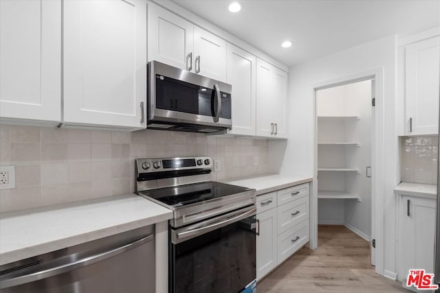 kitchen featuring white cabinets, light wood-type flooring, appliances with stainless steel finishes, and tasteful backsplash