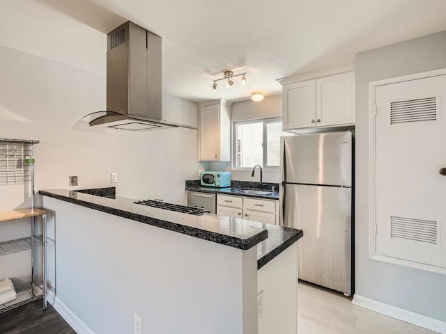 kitchen featuring sink, white cabinetry, island range hood, stainless steel fridge, and kitchen peninsula