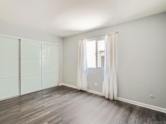 unfurnished bedroom featuring a closet, wood finished floors, and baseboards