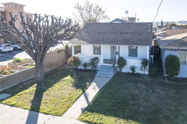 bungalow-style home with roof with shingles, a front yard, and fence