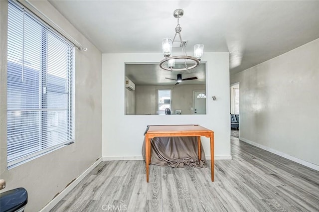 dining space featuring wood finished floors, a chandelier, baseboards, an AC wall unit, and a ceiling fan