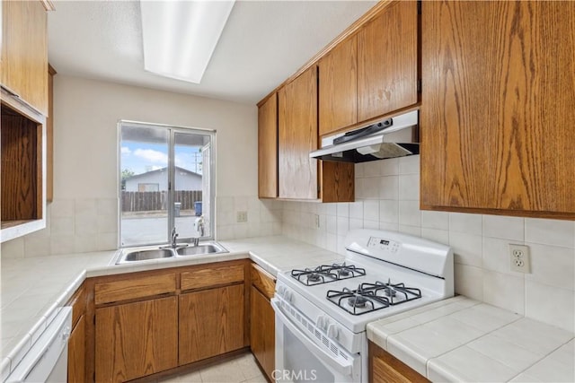 kitchen with white appliances, under cabinet range hood, tile countertops, and a sink