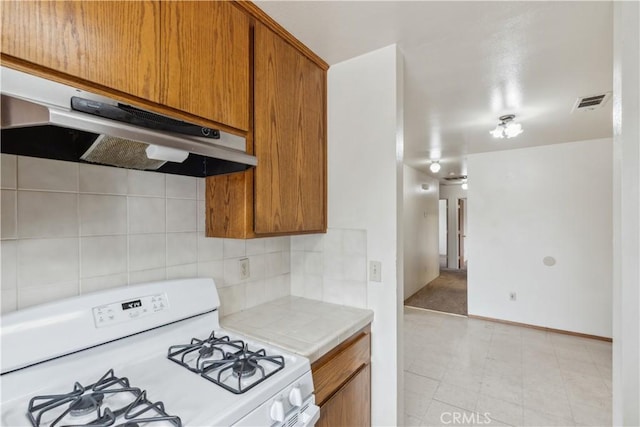 kitchen with white gas range, under cabinet range hood, brown cabinets, and decorative backsplash
