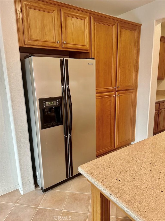 kitchen featuring light tile patterned floors, light stone countertops, and stainless steel refrigerator with ice dispenser