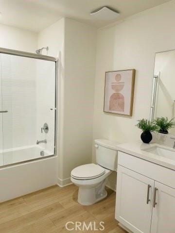 bathroom featuring visible vents, toilet, enclosed tub / shower combo, wood finished floors, and vanity