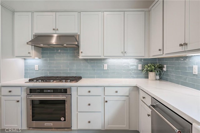 kitchen featuring light stone countertops, white cabinets, extractor fan, stainless steel appliances, and decorative backsplash