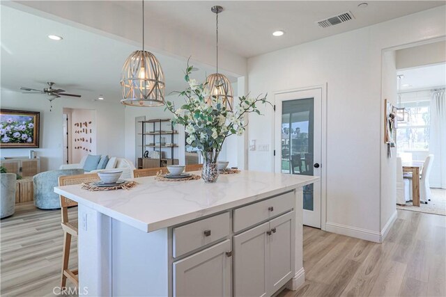 kitchen featuring light stone countertops, pendant lighting, a center island, a breakfast bar, and light hardwood / wood-style flooring