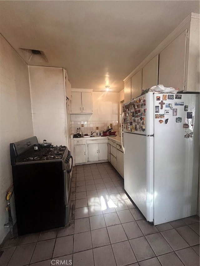 kitchen with white cabinets, decorative backsplash, dark tile patterned floors, white fridge, and stainless steel range with gas stovetop