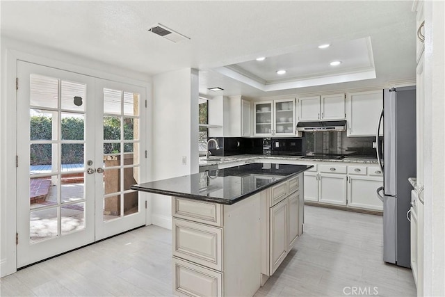 kitchen with a tray ceiling, dark stone countertops, a kitchen island, black appliances, and decorative backsplash