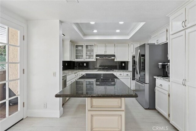 kitchen with appliances with stainless steel finishes, backsplash, dark stone counters, a tray ceiling, and a kitchen island