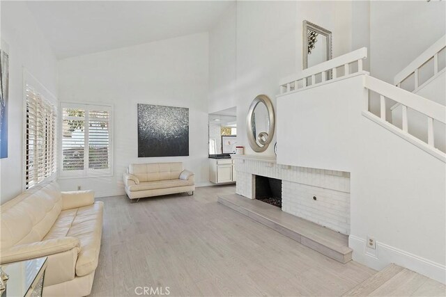 living room with high vaulted ceiling, a fireplace, and light wood-type flooring