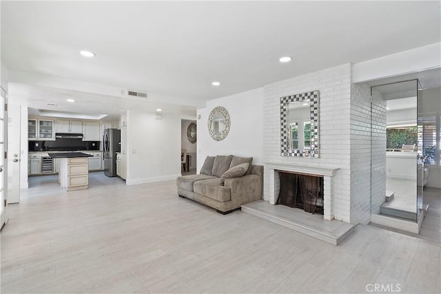 living room featuring a brick fireplace and light wood-type flooring