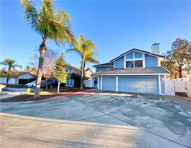 view of front facade featuring concrete driveway, a tile roof, fence, and a chimney