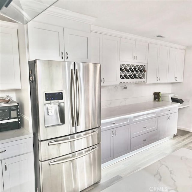 kitchen featuring light countertops, light wood finished floors, stainless steel refrigerator with ice dispenser, and white cabinetry