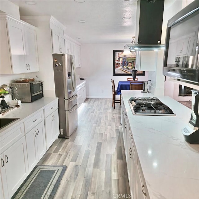 kitchen with light wood-style flooring, stainless steel appliances, white cabinets, light stone countertops, and decorative light fixtures