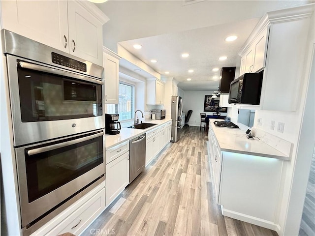 kitchen featuring stainless steel appliances, recessed lighting, light wood-style floors, white cabinetry, and a sink