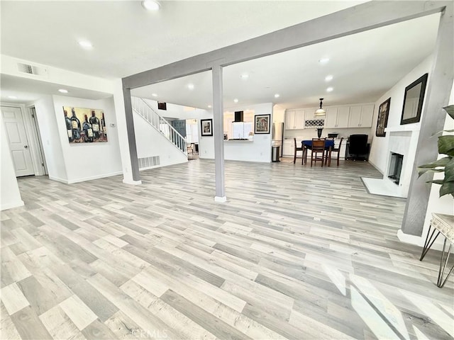 living room featuring a fireplace, recessed lighting, visible vents, light wood-style flooring, and stairs