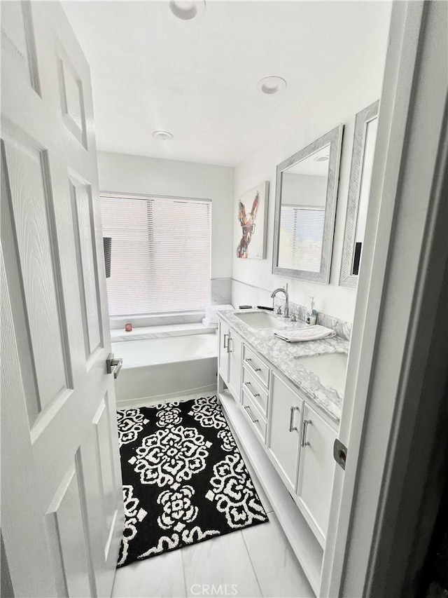 full bath featuring a healthy amount of sunlight, double vanity, a sink, and a bath