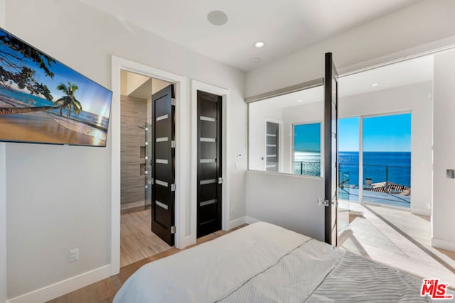 bedroom with light hardwood / wood-style floors, a water view, and access to outside