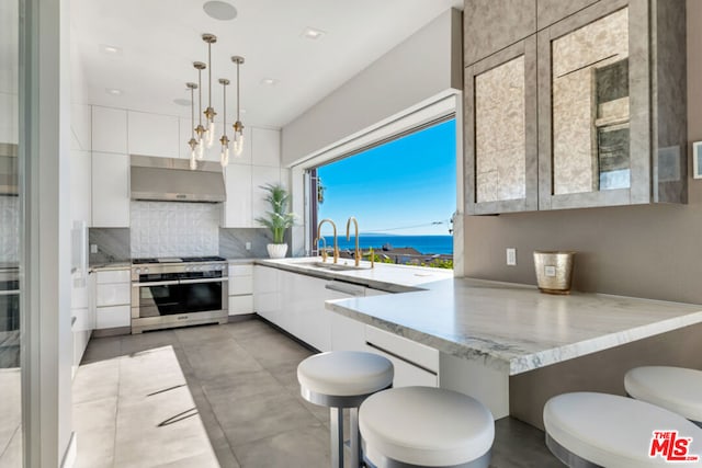 kitchen with exhaust hood, hanging light fixtures, white cabinets, a water view, and double oven range