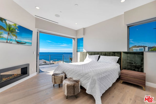 bedroom with light wood-type flooring, a water view, and access to outside