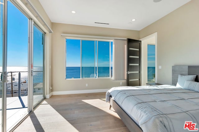 bedroom with a water view, access to outside, multiple windows, and wood-type flooring