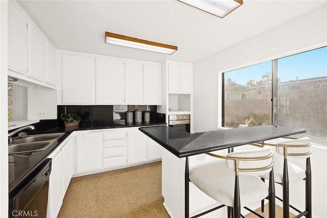 kitchen with sink, black dishwasher, white cabinets, a kitchen bar, and stainless steel oven