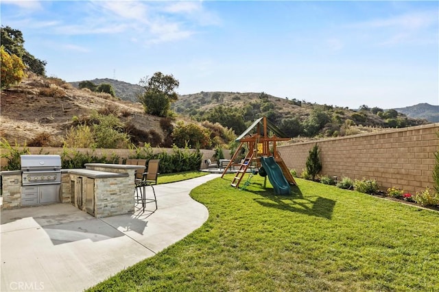 view of yard with a playground, a patio, a mountain view, exterior kitchen, and an outdoor bar