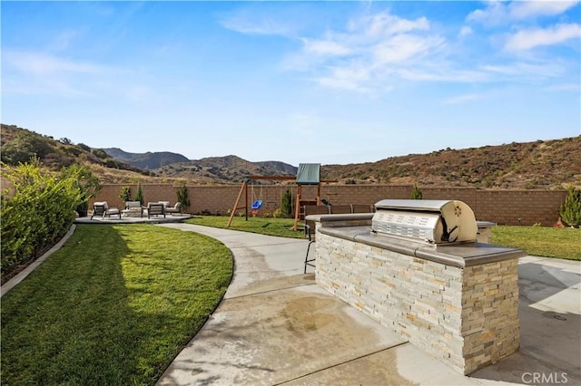 view of patio with a mountain view, a playground, an outdoor kitchen, and grilling area