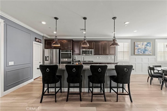 kitchen featuring light stone countertops, appliances with stainless steel finishes, a kitchen island with sink, ornamental molding, and a breakfast bar