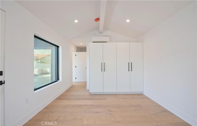 unfurnished bedroom featuring lofted ceiling with beams, a wall unit AC, and light wood-type flooring