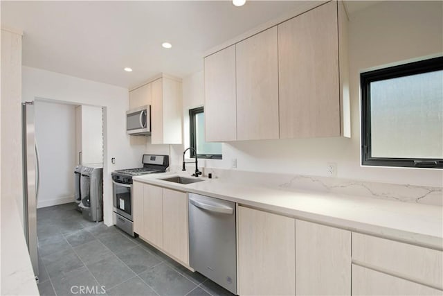 kitchen with appliances with stainless steel finishes, sink, light brown cabinets, and washing machine and clothes dryer