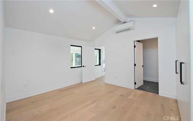 spare room featuring lofted ceiling with beams, an AC wall unit, and light wood-type flooring