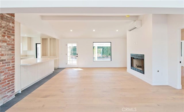 unfurnished living room featuring beam ceiling, light wood-type flooring, a wall mounted AC, and a fireplace