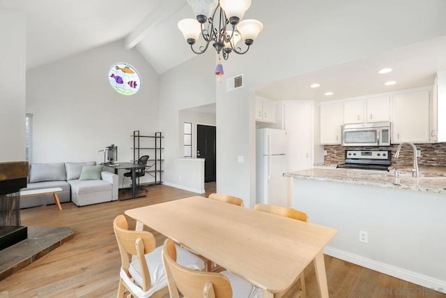 dining space with sink, light hardwood / wood-style flooring, a chandelier, and beamed ceiling